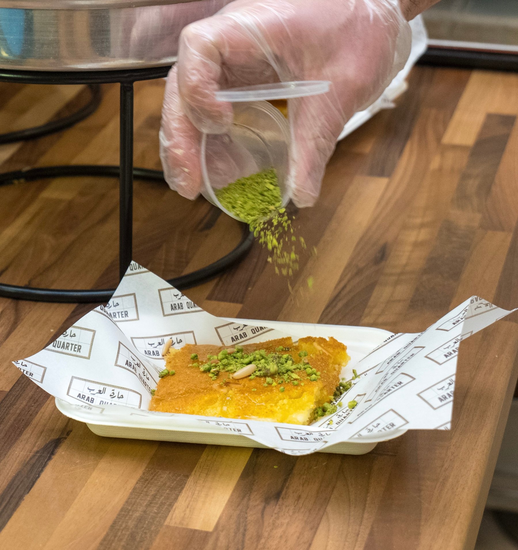 Pistachio being sprinkled over a serving of kunafa