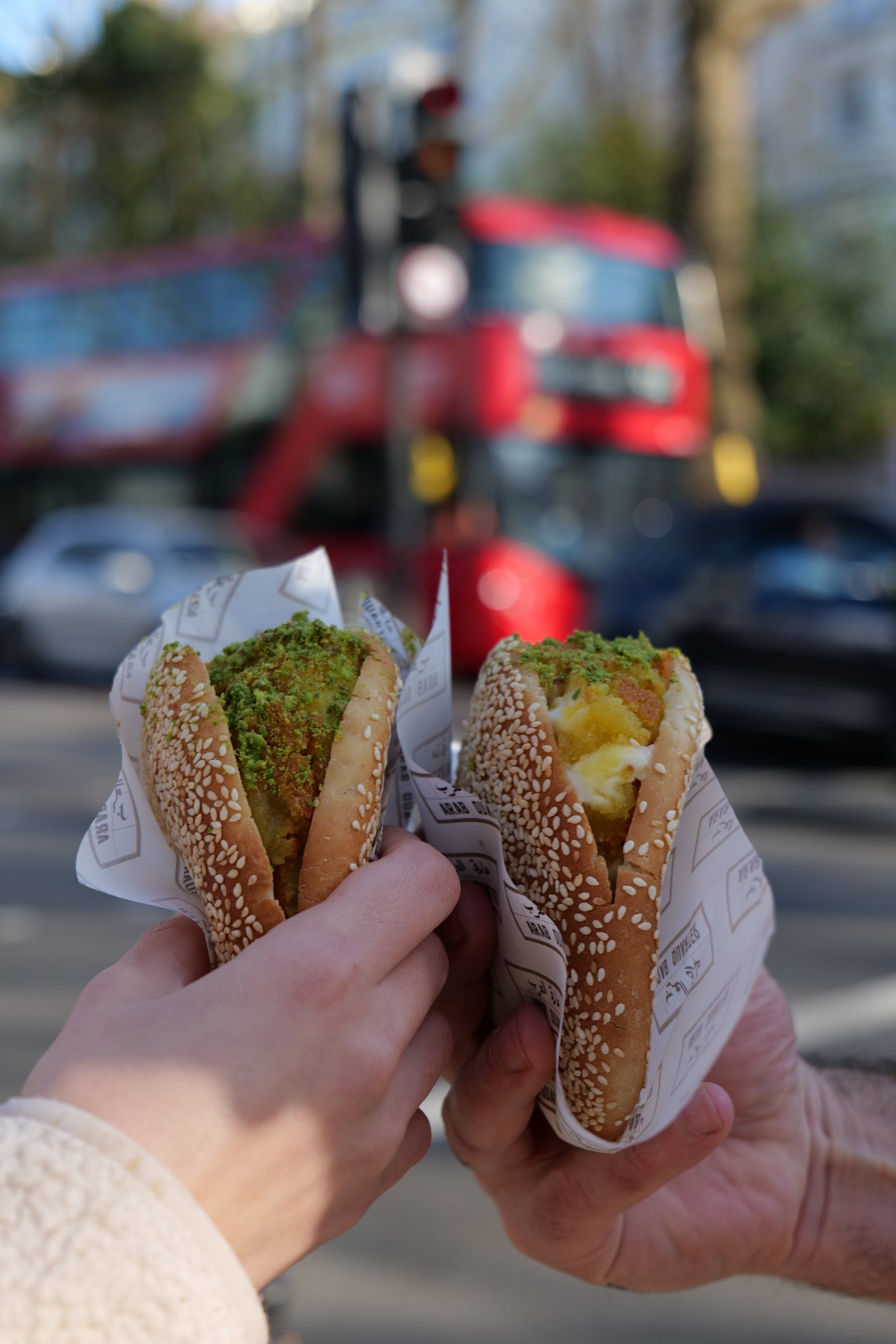 Two kunafa sandwiches in sesame buns held up on Holland Park Avenue